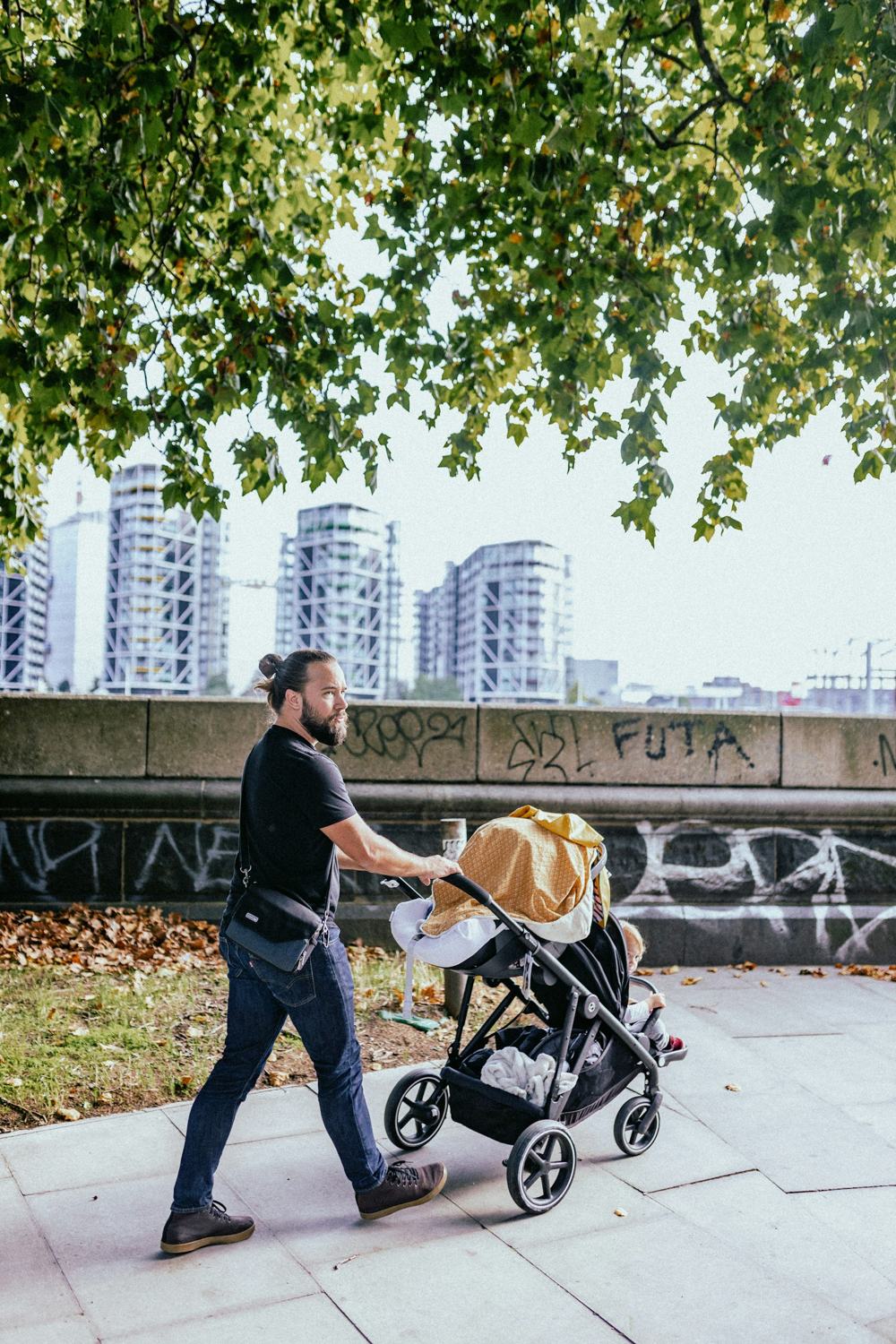 Een man loopt met een kinderwagen door de stad.