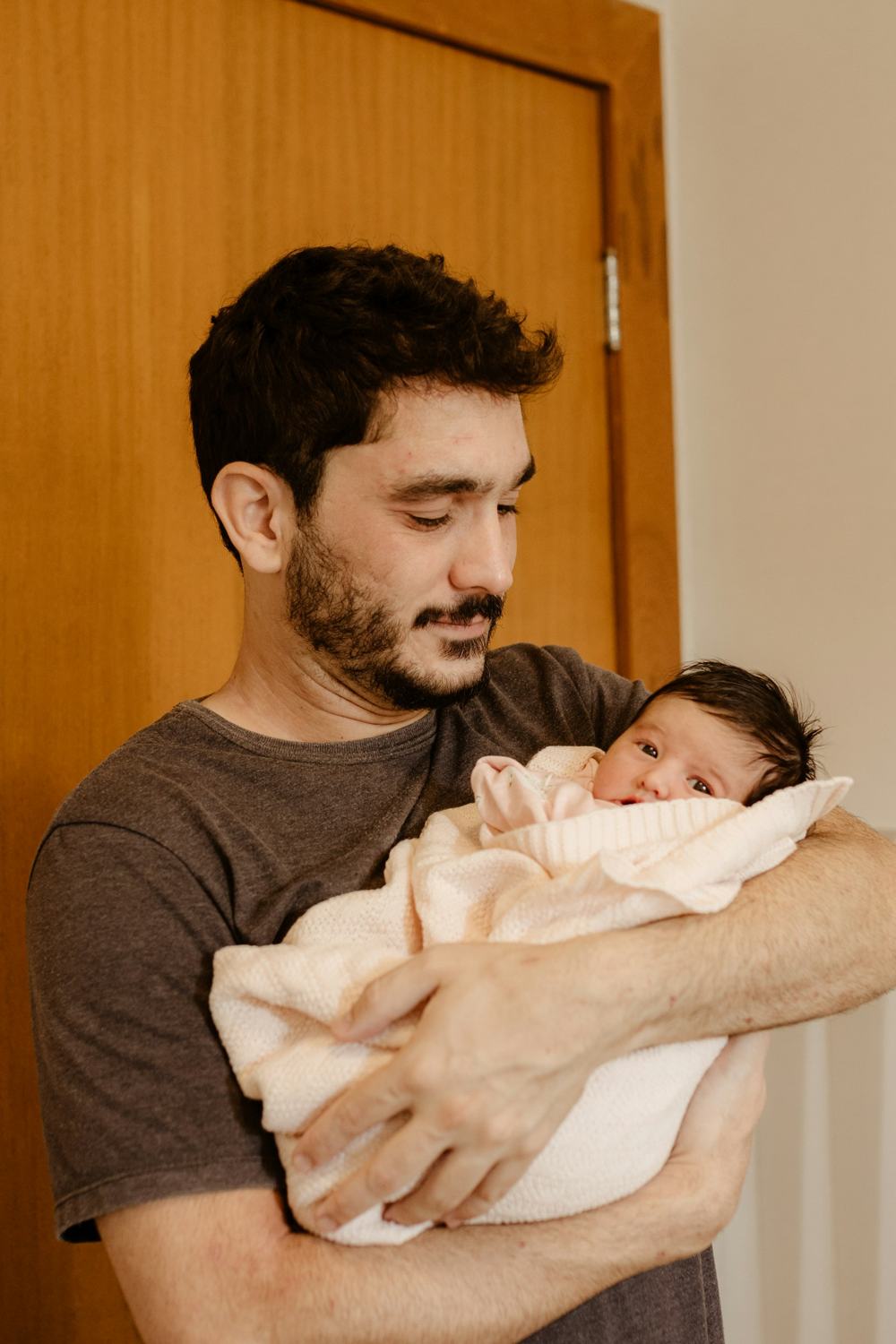 Een man met krullen en baard houdt zijn wakkere baby in zijn armen.